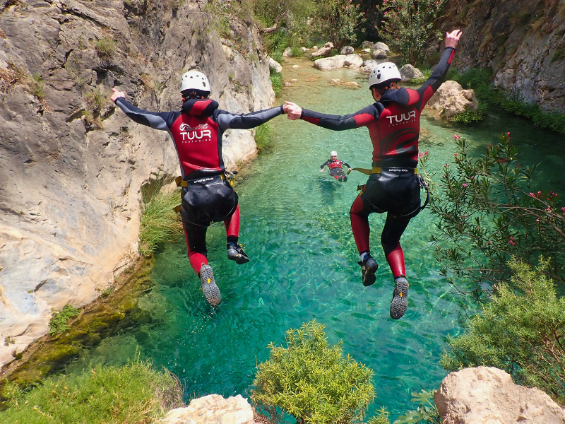 A couple jumping together into the green, crystal clear waters of the Rio Verde